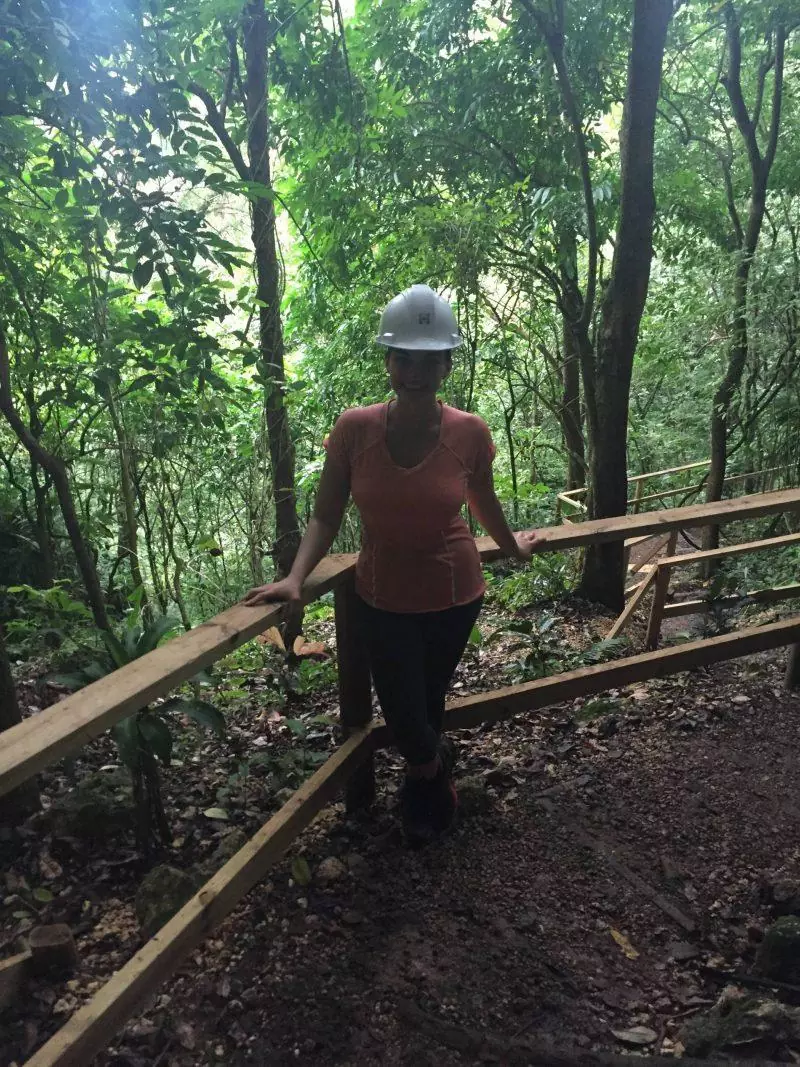 Woman wearing helmet standing by railing in forest