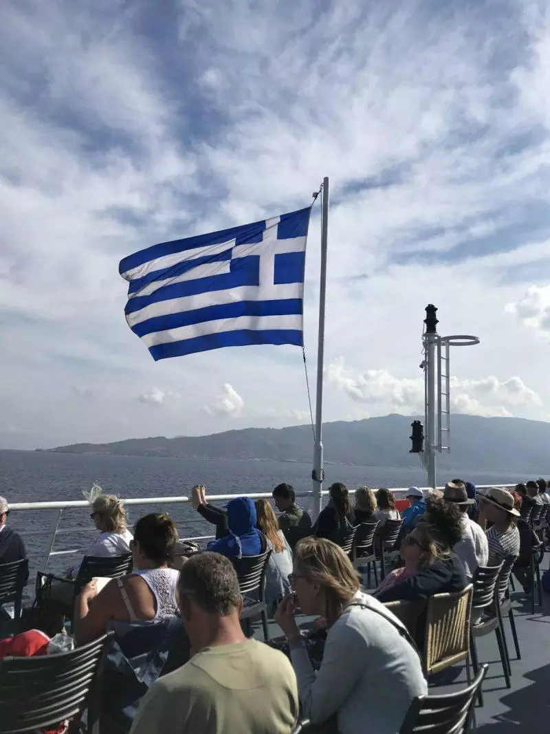 Passengers sitting on a ferry with waving Greek flag