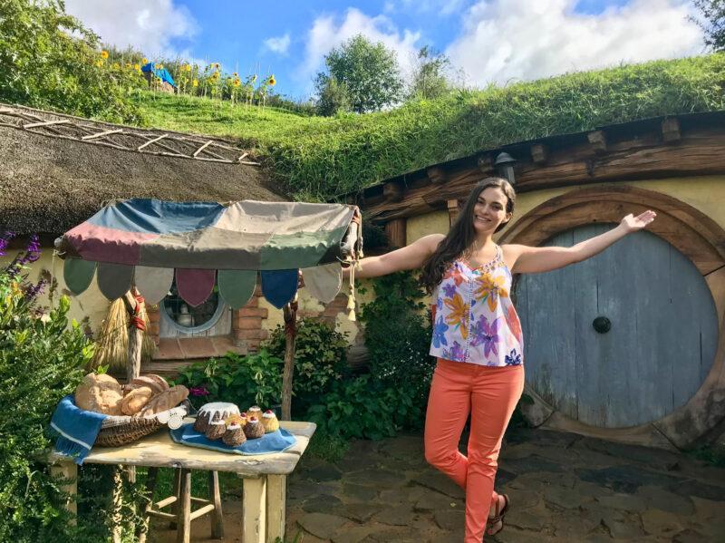 Woman standing in front of hobbit house with arm outstretched