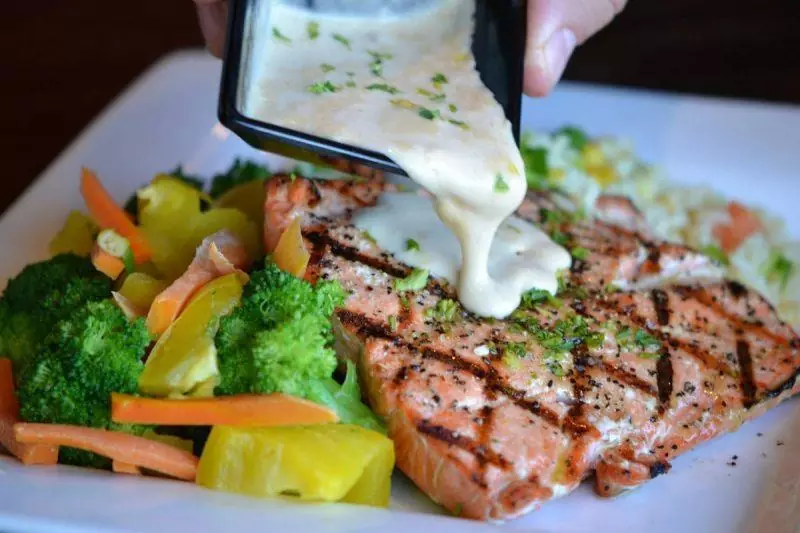 Pouring sauce over grilled salmon with a side of vegetables