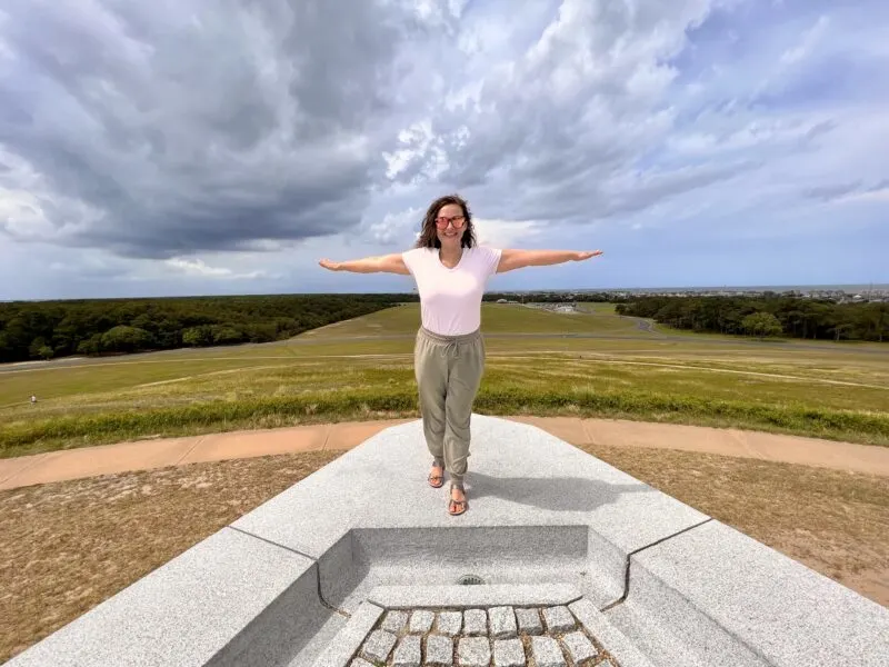 Woman standing at edge of Wright Memorial with arms out
