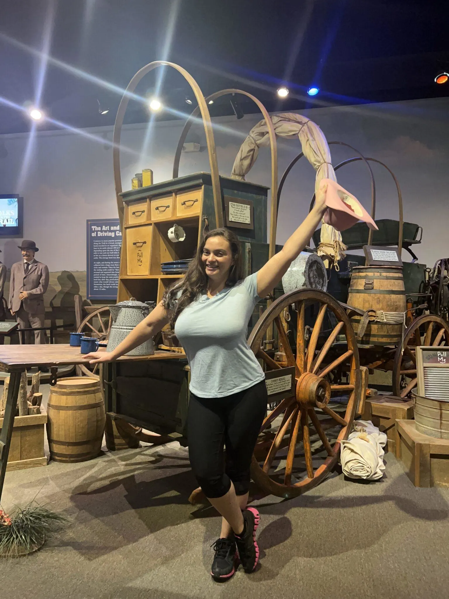Woman holding cowgirl hat and standing in front of wagon in museum