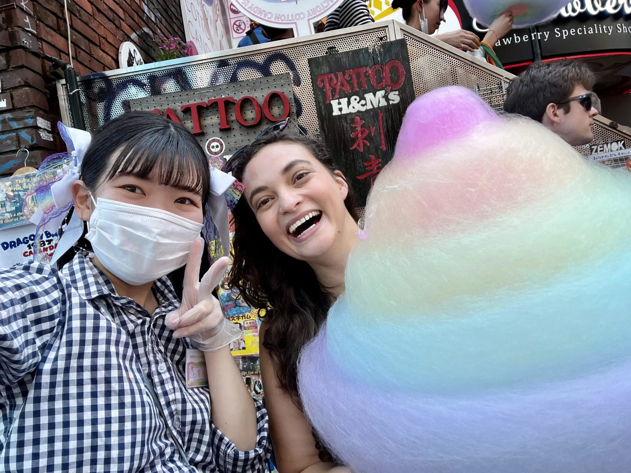 Woman holding giant cotton candy while standing next to store attendant giving peace sign