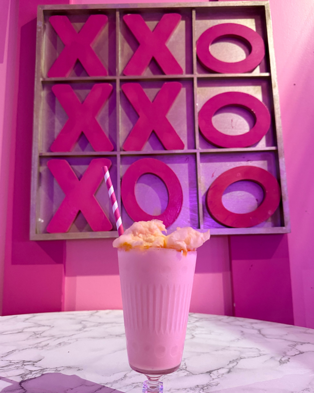Pink milkshake with cotton candy on top in front of tic tac toe board