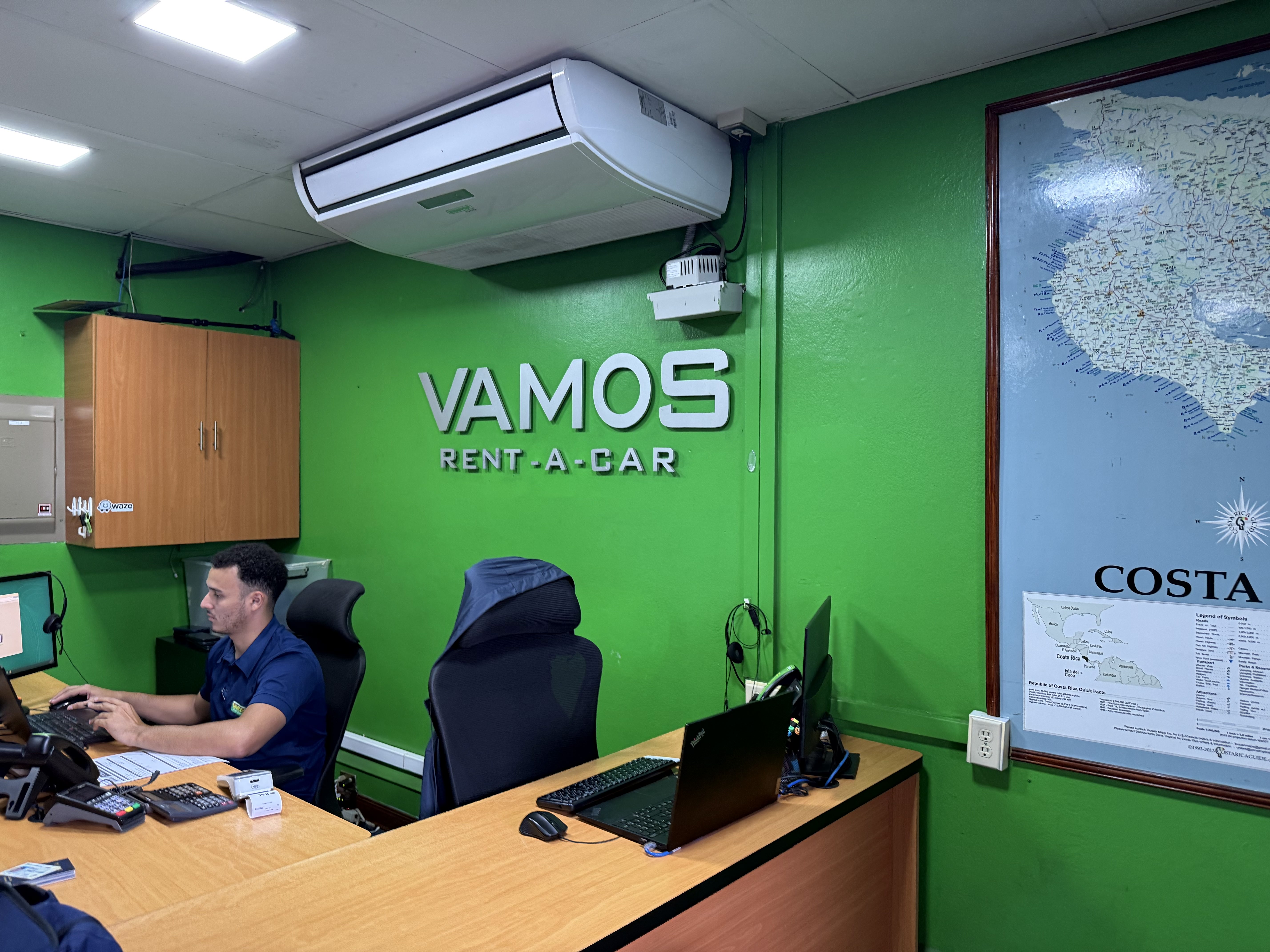 Green wall of rental car office with office name in center and map hanging in the corner