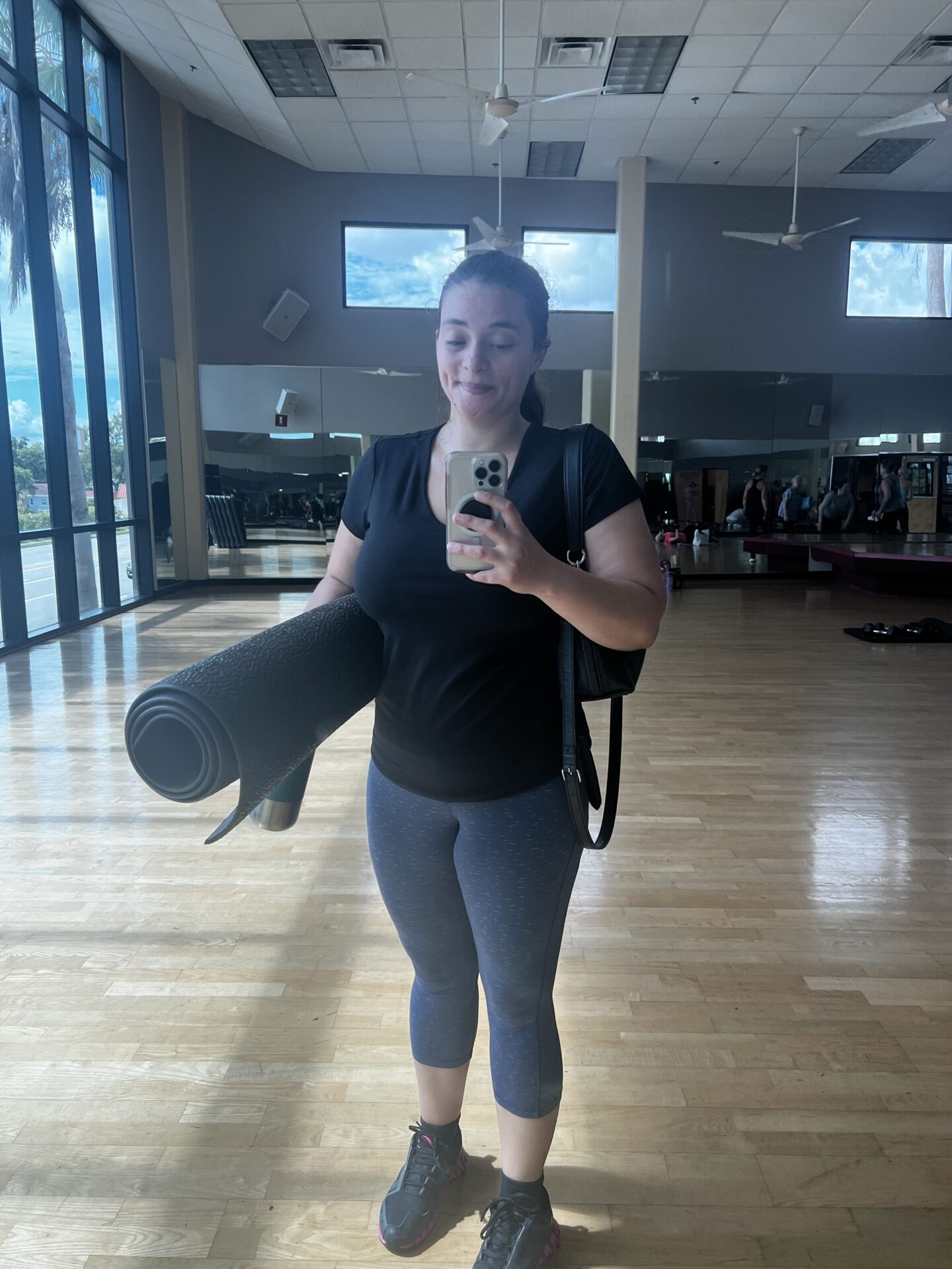 Woman taking gym selfie in the mirror while holding workout mat