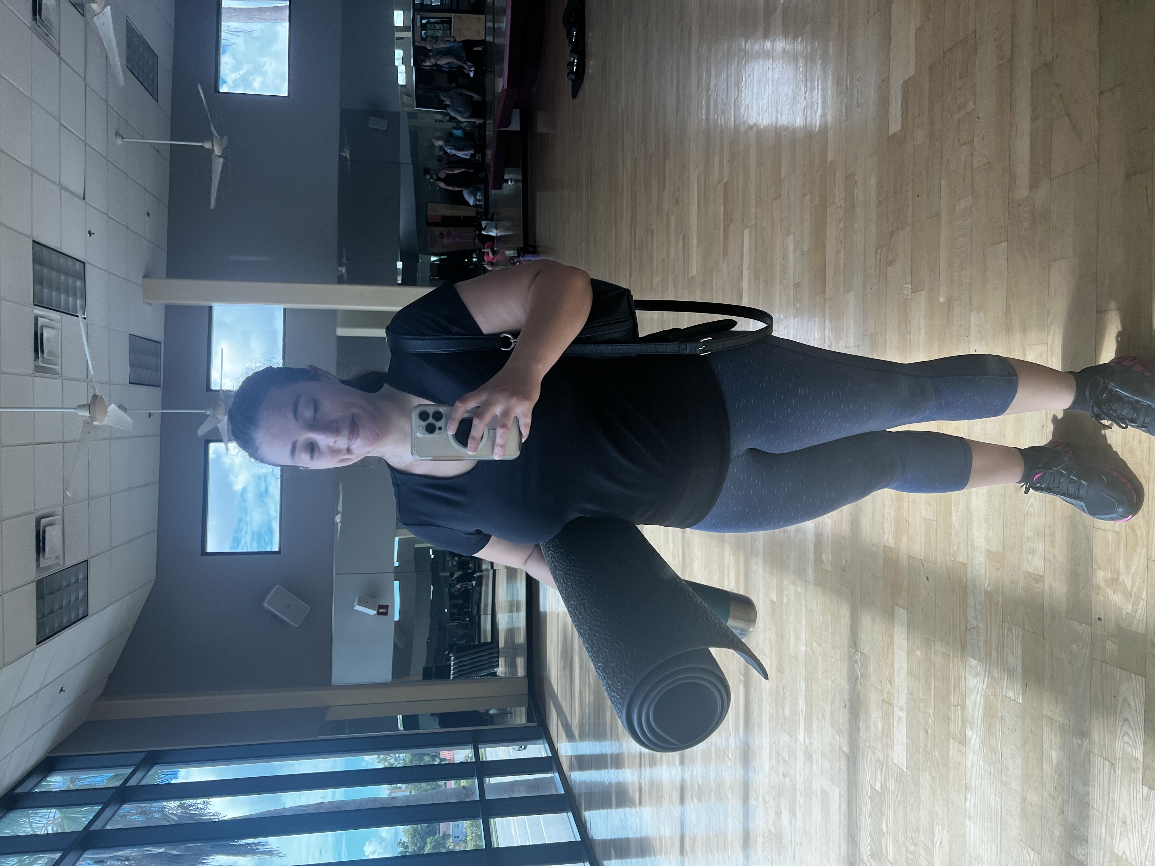 Woman taking gym selfie in the mirror while holding workout mat